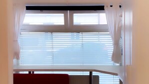 A room with a red sofa, a small table, a clock on the wall, and a window with blinds. - Innsbruck Apartment (Innsbruck)