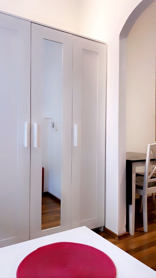 Une chambre avec un lit, un oreiller rouge, une armoire blanche et un bureau avec une chaise.