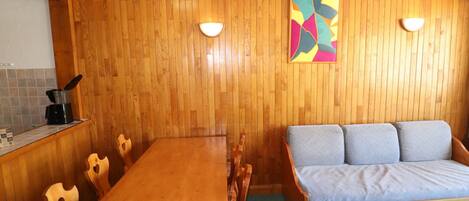 A wooden-paneled room with a dining table and chairs, a sofa, and a colorful abstract painting on the wall.