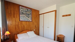 Une chambre avec une tête de lit en bois, un lit avec une literie blanche, une table de chevet avec une lampe, une armoire en bois et une petite table en bois.