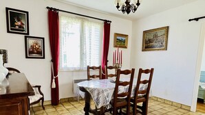 A dining area with a round table, wooden chairs, a chandelier, and a window with curtains. - T3 House in Cambo, Pets Allowed, Parking, Internet (Cambo-les-Bains)