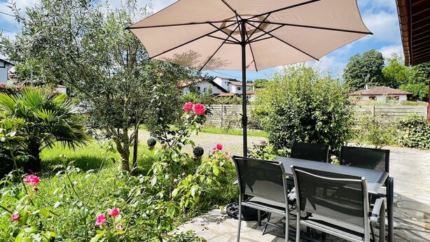 An outdoor patio with a table and chairs, a large umbrella, and surrounding greenery. - T3 House in Cambo, Pets Allowed, Parking, Internet (Cambo-les-Bains)