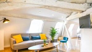Ein modernes Wohnzimmer mit einem grauen Sofa, gelb-blauen Kissen, einem Holztisch und einem blauen Sessel.
