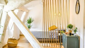 Ein gemütliches Schlafzimmer im Loft-Stil mit schrägem Dach, einem Bett mit gelbem Kissen, einem grünen Metallschreibtisch und einer hängenden Pflanze.