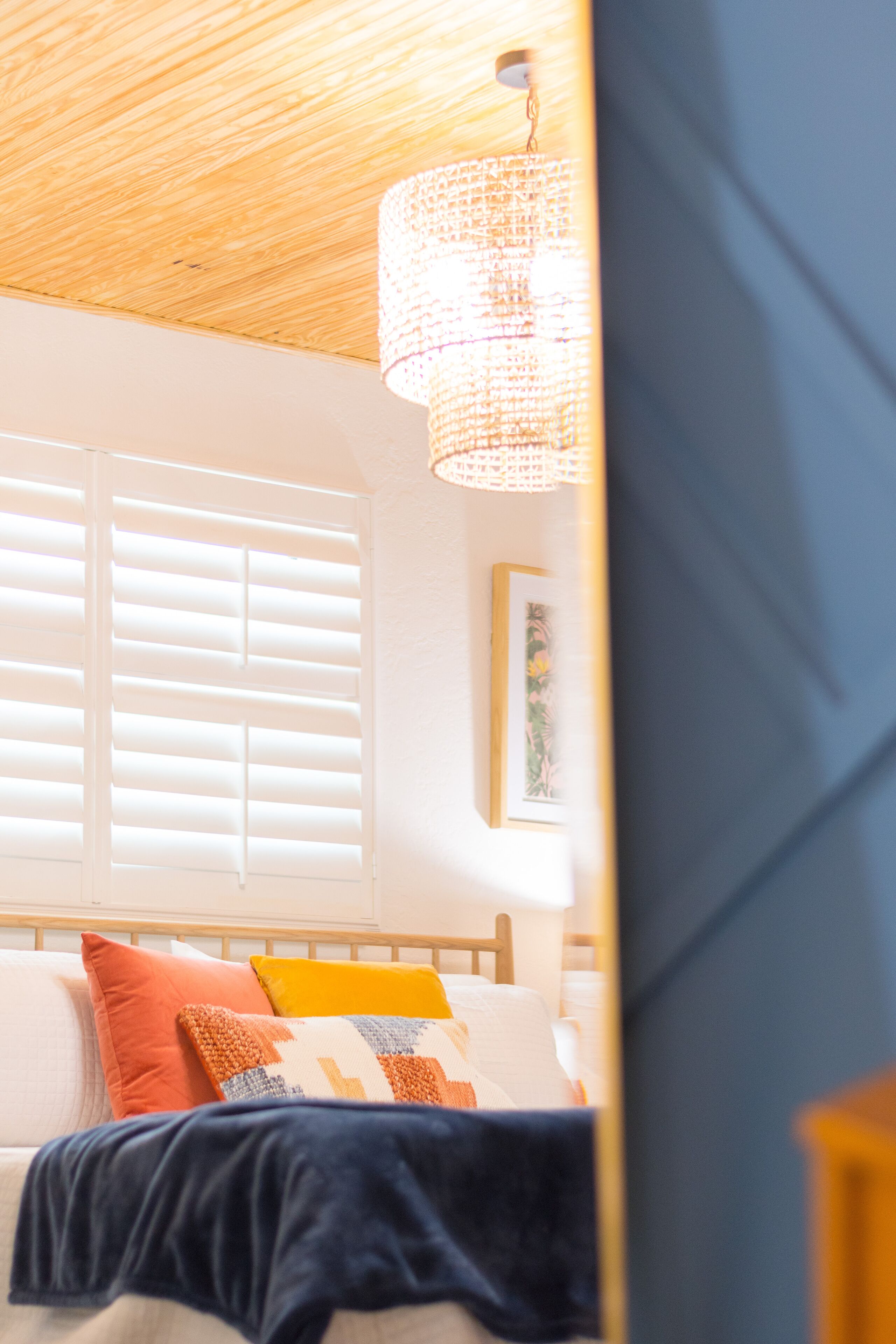 A bedroom with a wooden ceiling, a bed with multiple pillows, a hanging light fixture, and a window with blinds.