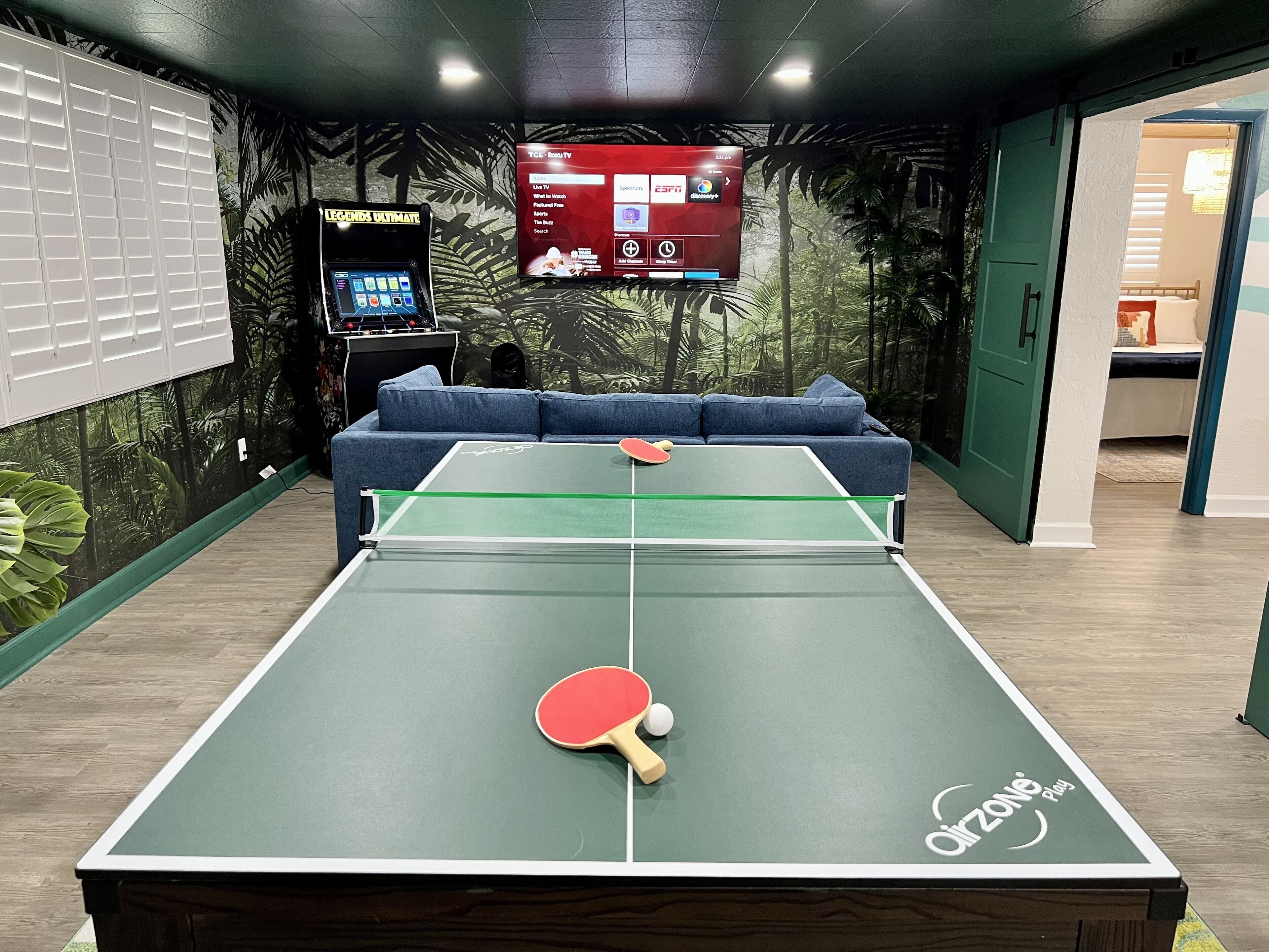 Una mesa de ping pong con un televisor montado en la pared mostrando varios canales.