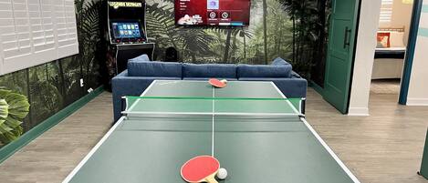 Una mesa de ping pong con un televisor montado en la pared mostrando varios canales.