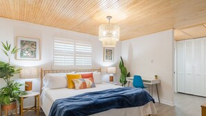 Un dormitorio con techo de madera, una cama con manta azul, dos mesitas de noche con lámparas, un escritorio y una silla.