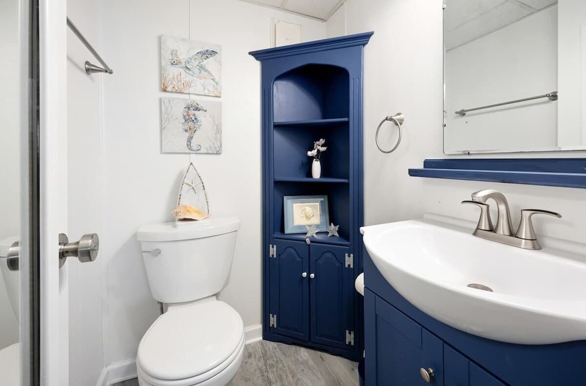 A bathroom with a white toilet, a blue cabinet with shelves, and a white sink.