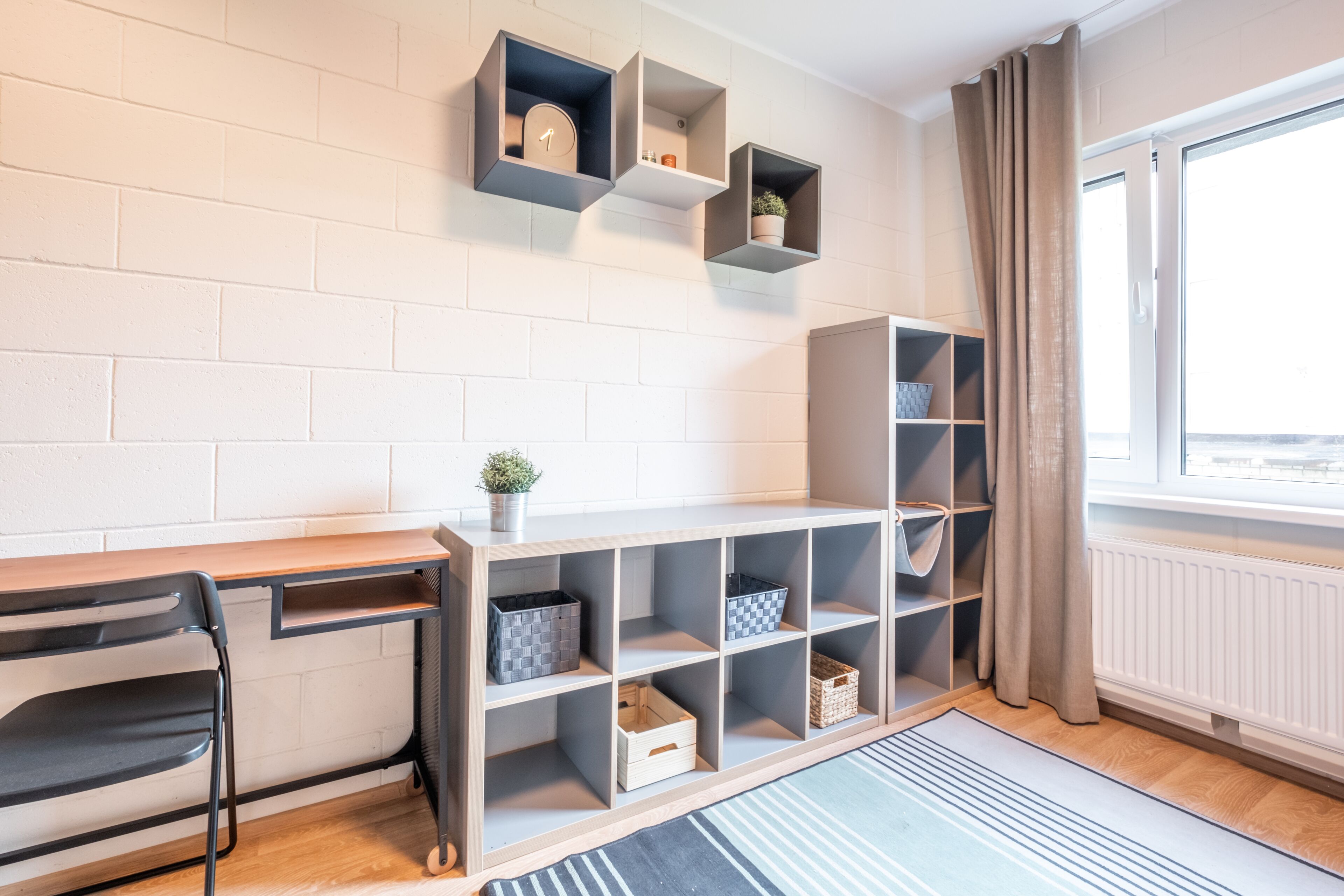 A modern room with a wooden desk, black chair, and open shelving with storage bins.