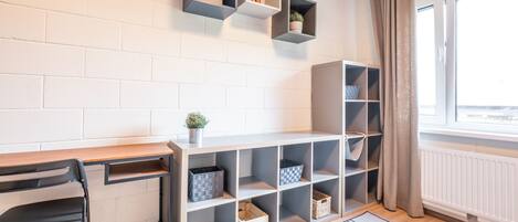 A modern room with a wooden desk, black chair, and open shelving with storage bins.