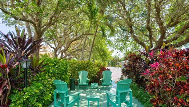 An outdoor seating area with green chairs and a table, surrounded by lush greenery and trees. - 2 beds, Kitchenette, Free Parking - Room 2 (Tequesta)