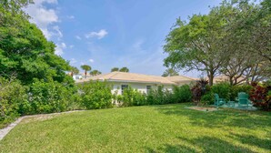 A house with a well-maintained lawn, a patio with outdoor furniture, and a variety of trees and shrubs. - 2 beds, Kitchenette, Free Parking - Room 2 (Tequesta)