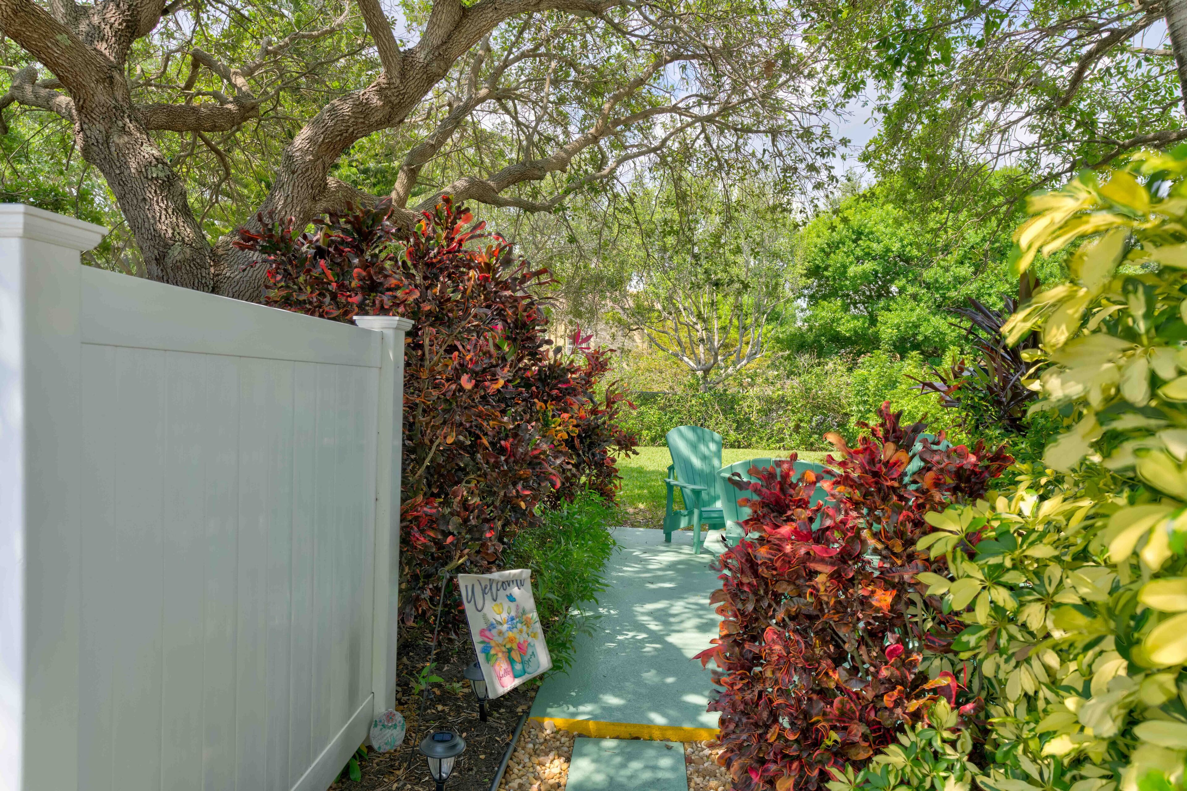 A garden pathway leading to a seating area with a white fence and lush foliage.