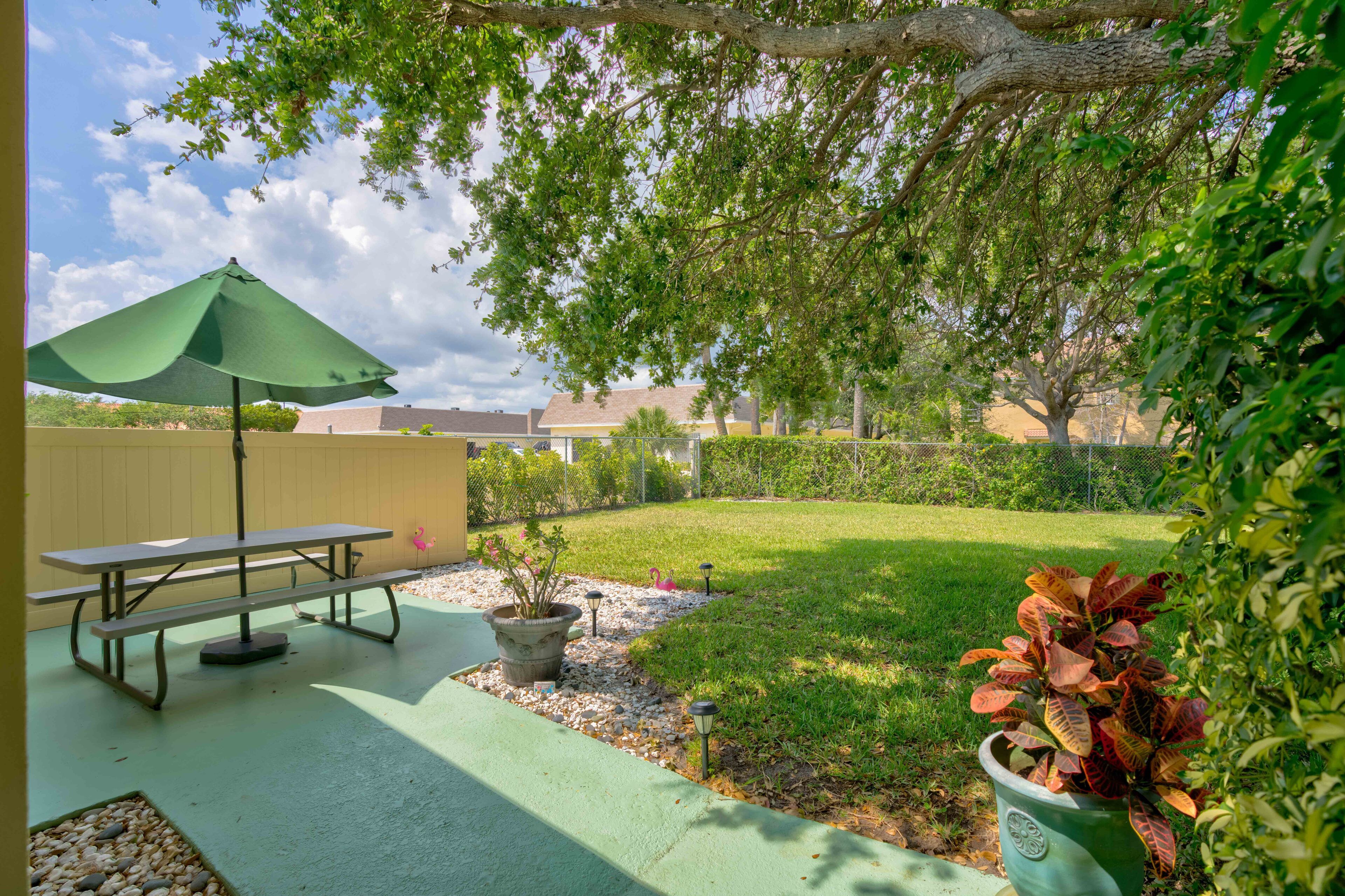 A patio with a picnic table and umbrella, surrounded by a well-maintained lawn and a fence.