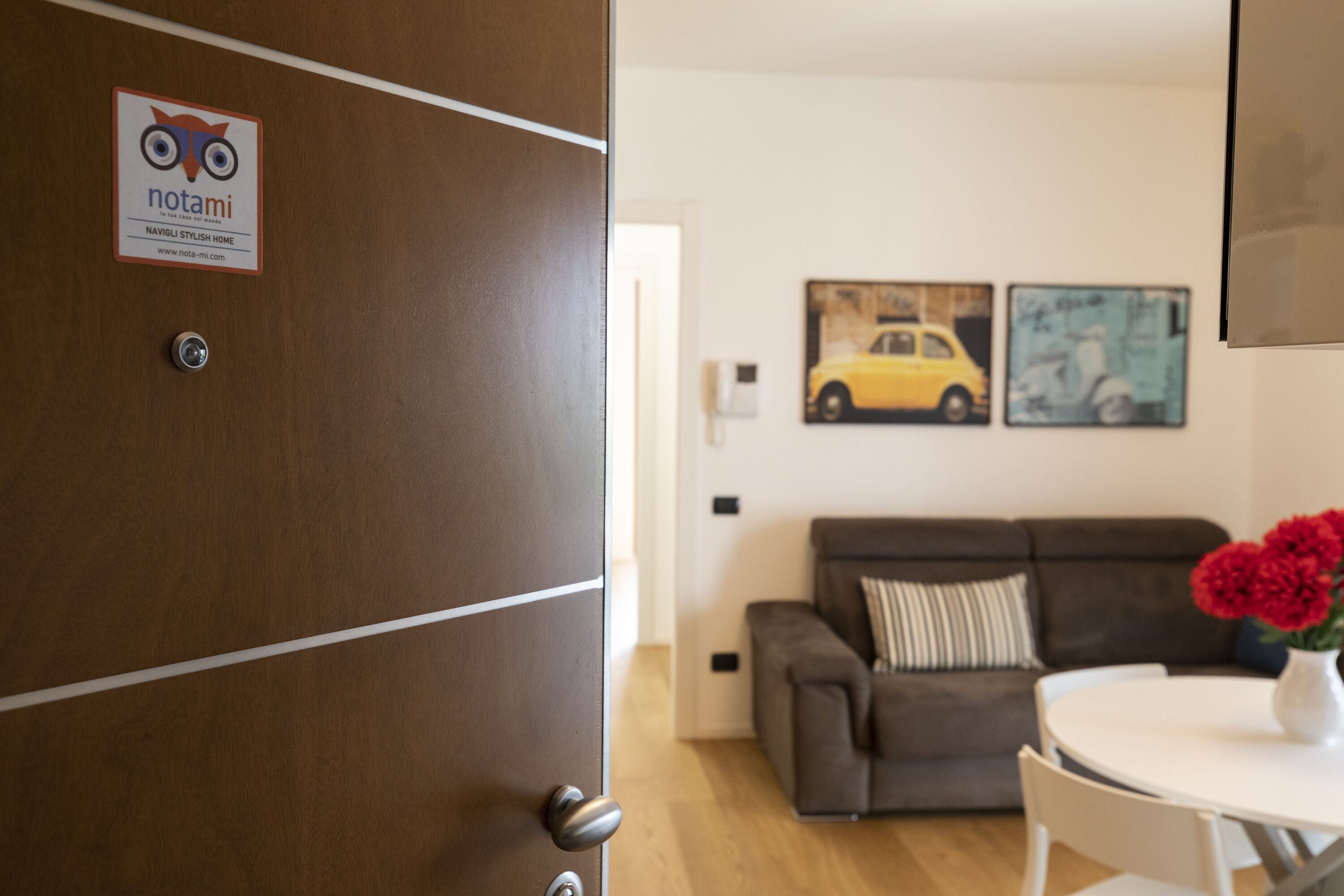 Un interior modern amb una porta de fusta, un sofà, una taula amb flors i dues obres d'art murals.