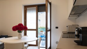 A modern kitchen with a coffee machine, a dining table with chairs, and a view of the outdoors through a sliding door.