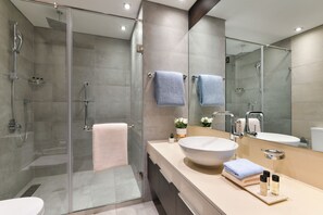 A modern bathroom with a glass-enclosed shower, a large mirror, and a beige vanity with a white sink and two towels.