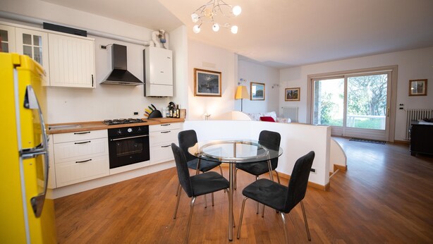 A modern kitchen with white cabinets, a yellow refrigerator, and a round glass table with four chairs. - Casa Vacanze Cecilia (Manerba del Garda)