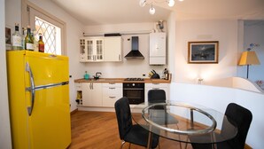 A compact kitchen with a yellow refrigerator, white cabinets, and a glass dining table with black chairs. - Casa Vacanze Cecilia (Manerba del Garda)