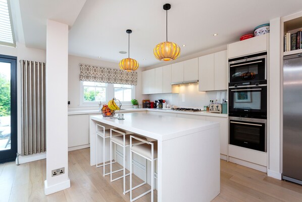 A modern kitchen with a central island, pendant lighting, built-in ovens, and a view to the outdoors.