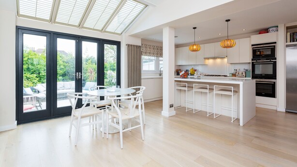 Een moderne keuken met een centraal kookeiland, hanglampen en zicht op groen door grote ramen.