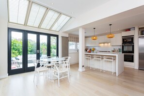 A modern kitchen with a central island, pendant lighting, and a view of greenery through large windows. - Wandsworth Idyll, by Veeve (London)