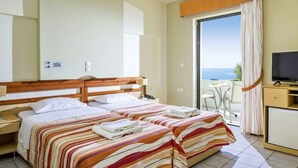Habitación de hotel con dos camas, televisión, escritorio y vista al mar.
