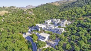 Vista aérea de un moderno resort con varias edificaciones blancas, rodeado de exuberante vegetación y montañas al fondo.