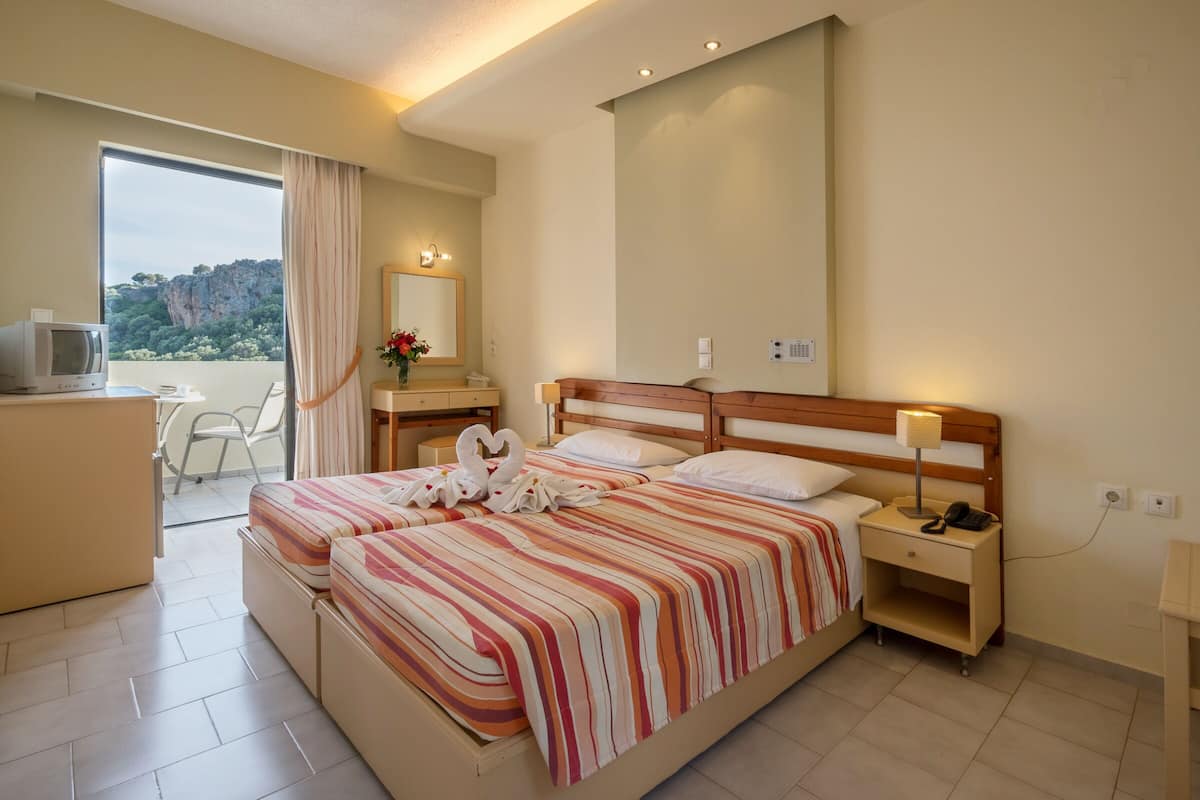 A hotel room with a bed, bedside table, lamp, and a view of a mountainous landscape through a large window.