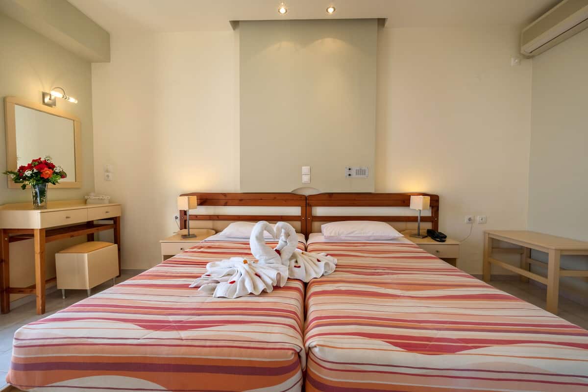 A hotel room with two beds, a wooden desk, a vanity with a mirror, and a vase of flowers.