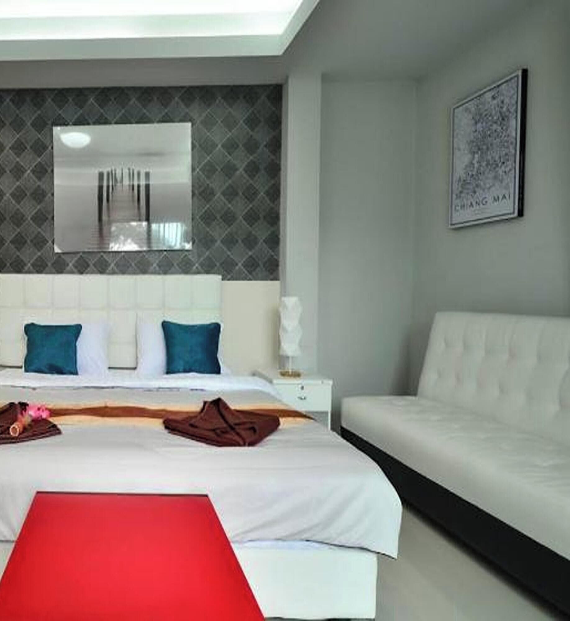 Ein Hotelzimmer mit einem Bett, einem weißen Sofa, einem roten Sessel, einem Nachttisch und einem wandmontierten Spiegel.