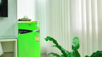 A room with a green refrigerator, a potted plant, and a television on the wall.