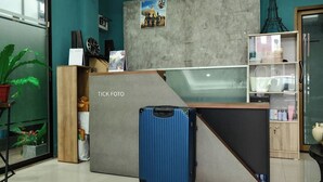 Een receptiebalie met een blauwe koffer ervoor, een klok en een lijst op de muur.