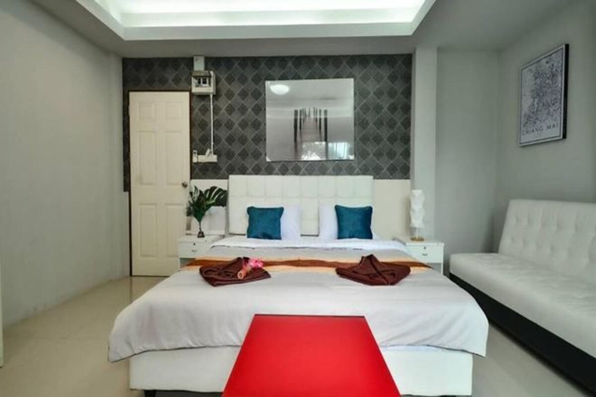 Ett hotellrum med en säng, en röd bänk, en vit soffa, en stor spegel och en dörr.