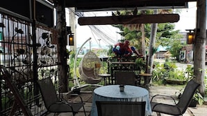 Een terras met een ronde tafel en stoelen, een hangstoel en een decoratieve metalen omheining.