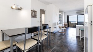Ein modernes Interieur mit einem Essbereich, der Metalltische und -stühle umfasst, einer Küchenzeile mit weißen Schränken und Blick durch ein großes Fenster.