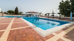 Ein Schwimmbecken mit gefliestem Sonnendeck, überdachter Sitzgelegenheit und Sonnenschirmen.