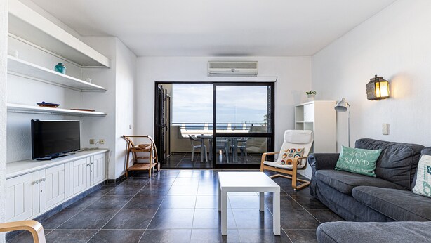 Ein modernes Wohnzimmer mit Flachbildfernseher, einem grauen Sofa, einem weißen Couchtisch und einem Balkon mit Blick.