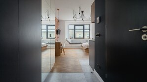 A modern bedroom with a large window, a wooden floor, and a bed with a white headboard.