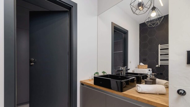 A modern bathroom with a dark door, a wooden countertop, a black sink, a mirror, and a towel rack.
