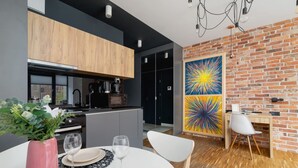 A modern kitchen with a wooden cabinet, a dining table set with plates and glasses, and a colorful abstract painting on the brick wall.