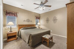Une chambre à coucher comprenant un lit, des tables de chevet, un ventilateur de plafond et des œuvres d’art décoratives accrochées au mur.