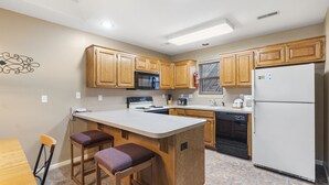 Una cocina con armarios de madera, una isla central con taburetes, microondas, estufa y refrigerador.