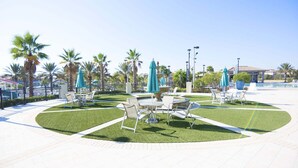Eine Außenpatio-Terrasse mit Tischen und Stühlen, umgeben von Palmen und einem Springbrunnen.