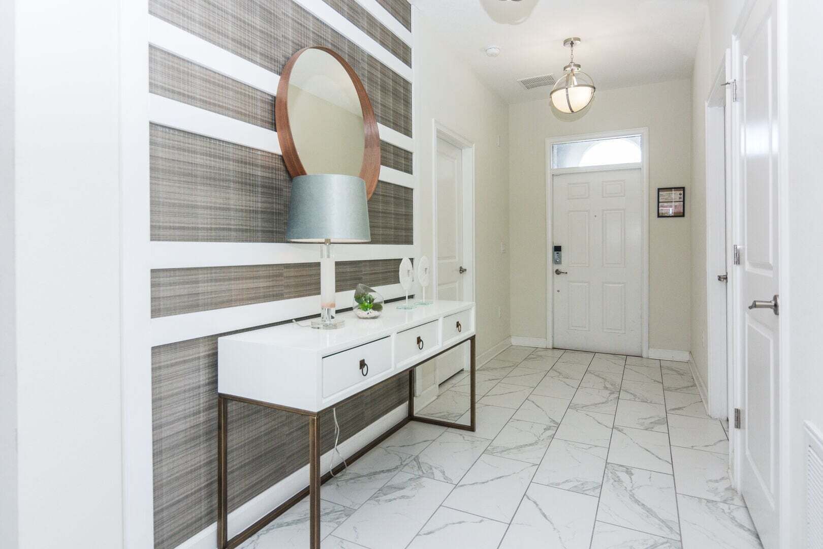 A hallway with a white console table, a mirror, a lamp, and a door.