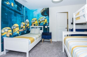 Une chambre avec un décor mural sur le thème des Minions, un lit superposé, une table de chevet et une commode.