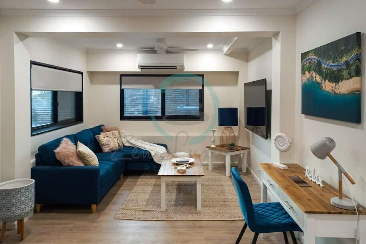 A modern living room with a blue sofa, a wooden desk, and a dining table.