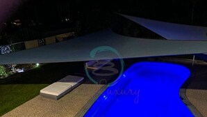 A swimming pool with a blue light, a covered area, and a small white bench. - ZEN AT ROSEWOOD - 2BR Guesthouse & Pool (Leanyer)