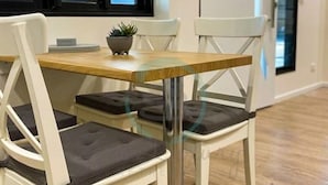 A dining area with a wooden table and white chairs with cushioned seats. - ZEN AT ROSEWOOD - 2BR Guesthouse & Pool (Leanyer)
